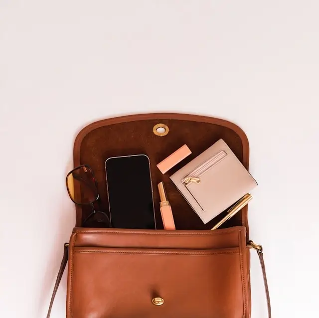 Open tan leather handbag showing contents including a phone, sunglasses, wallet and lipstick