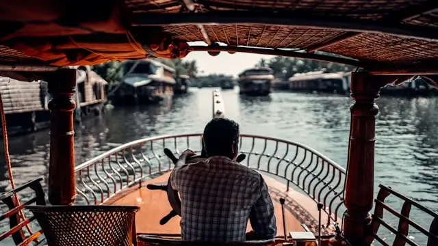 Man steering a wooden boat through a calm river waterway