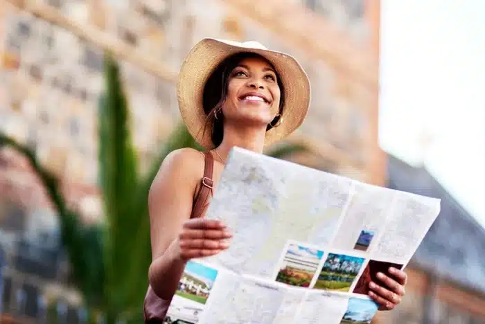 A young woman smiling and holding a travel map outdoors, embracing the perks of solo traveling