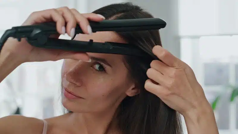 Woman straightening her hair with a flat iron at home