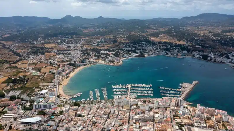 Aerial view of Sant Antoni de Portmany in Ibiza with a packed marina, turquoise bay, and mountain backdrop