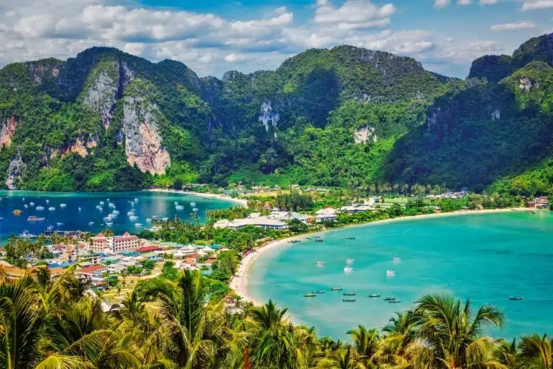 Turquoise waters and limestone peaks of the Andaman Sea coastline in Thailand with boats and beachside resort