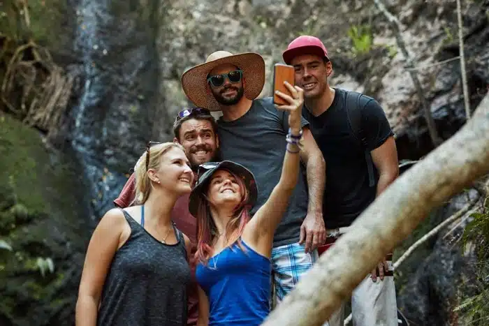 A group of solo travelers taking a selfie together on a jungle hike near a waterfall