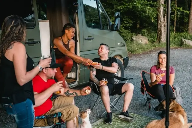 group of friends eating and sharing food outside a campervan during a road trip