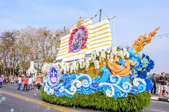 A decorated floral parade float shaped like a golden ship adorned with white and yellow flowers at the Chiang Mai Flower Festival in Thailand