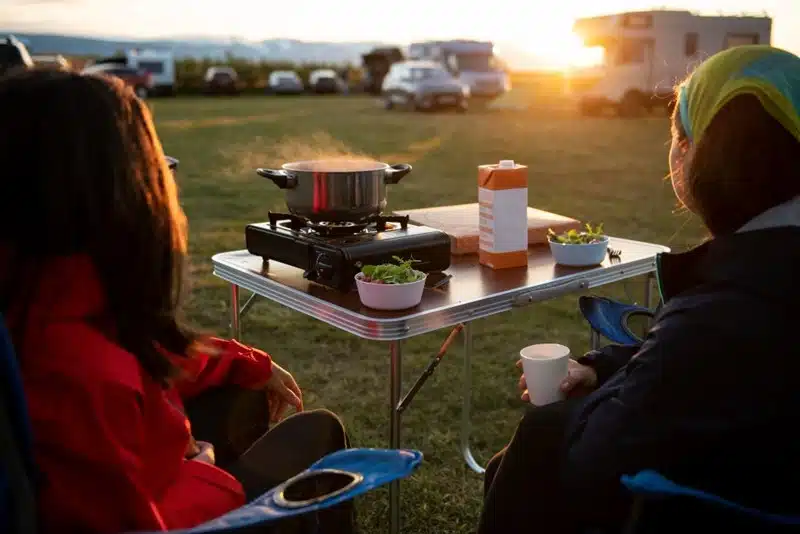 two campers cooking a meal on a portable stove at an rv campsite during sunset