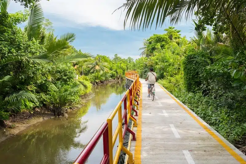 A cyclist riding across a narrow bridge over a canal surrounded by dense tropical greenery in Bang Krachao Bangkok