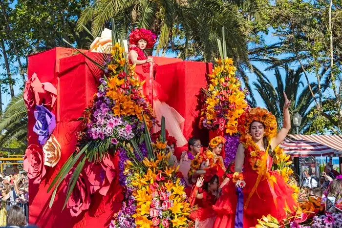 Dancers in red floral costumes performing on a vibrant float decorated with tropical blooms during the Madeira Flower Festival parade in Funchal, Portugal