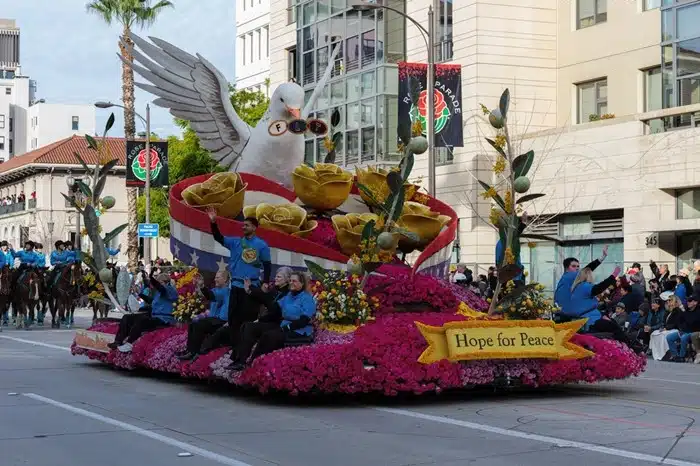 A "Hope for Peace" float featuring a large white dove and golden roses covered in pink flowers at the Rose Parade in Pasadena, California