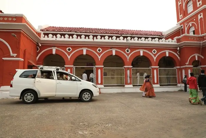 exterior of a government hospital in India with people and a parked car outside