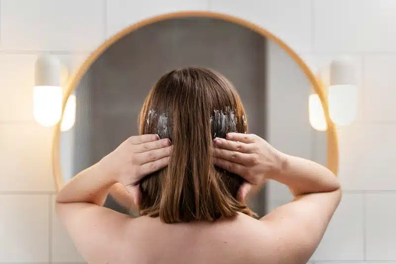 Woman applying a hair mask in front of a bathroom mirror
