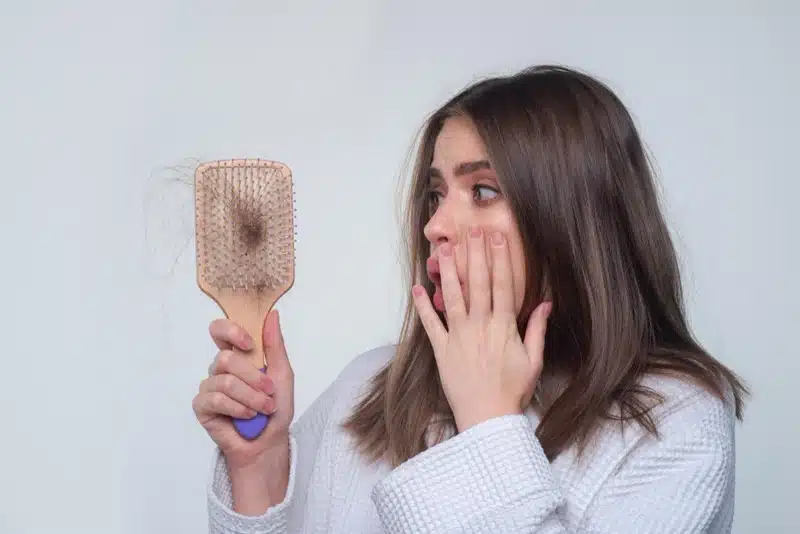 Woman looking at hair loss on her brush with a shocked expression