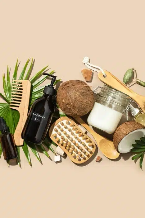 Natural haircare products with coconut oil, wooden comb, and brush on a beige background