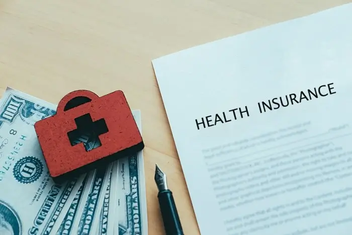 health insurance policy document with first aid kit and cash on a wooden table