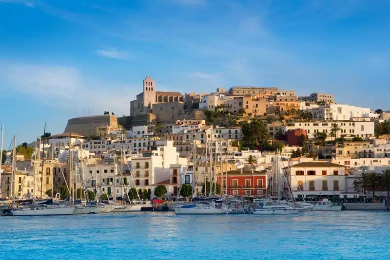 Ibiza Eivissa old town viewed from the water with sailboats docked along the harbour at golden hour