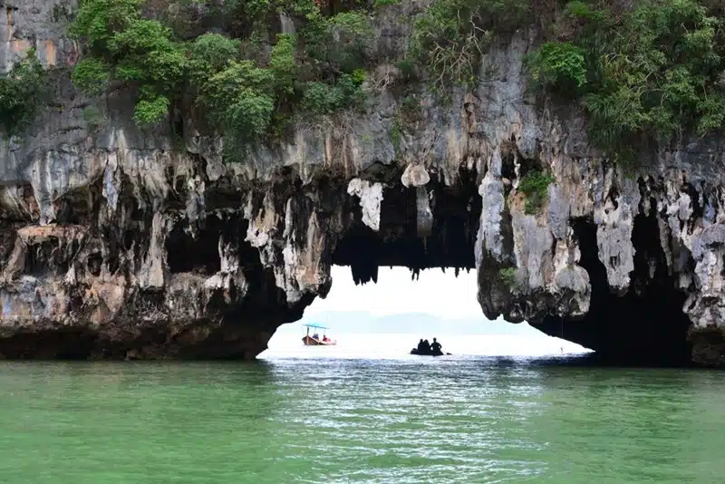 Travelers kayaking through a narrow sea cave in Phang Nga Bay surrounded by towering karst rock formations