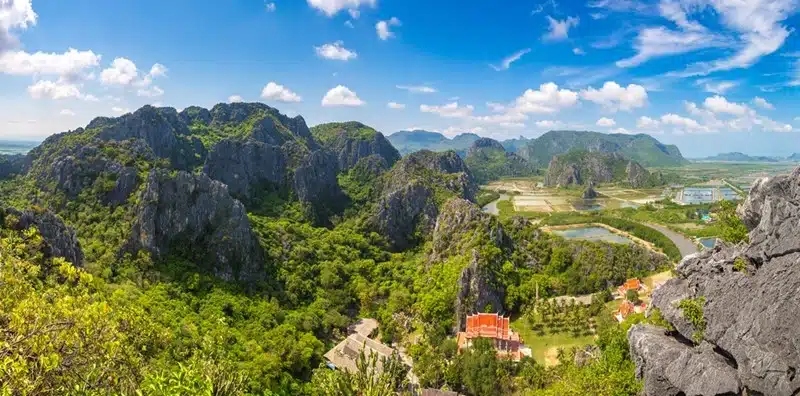 Panoramic view of Khao Sam Roi Yot National Park in Thailand with jagged limestone peaks, lush greenery, and a red-roofed temple below