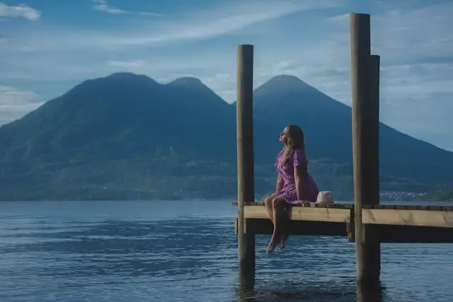 Woman sitting peacefully on a wooden dock overlooking Lake Atitlán with volcanic mountains in the background, Guatemala