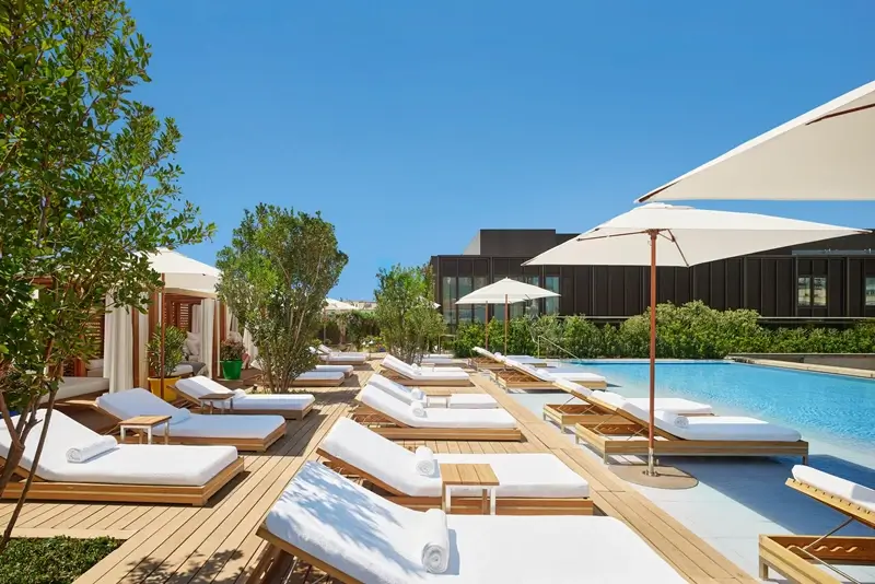 Clean and modern EDITION hotel outdoor pool area with wooden deck and white lounge chairs
