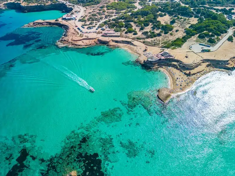 Aerial view of Platges de Comte in north Ibiza with vivid turquoise waters, rocky coastline, and a speedboat cutting through the sea