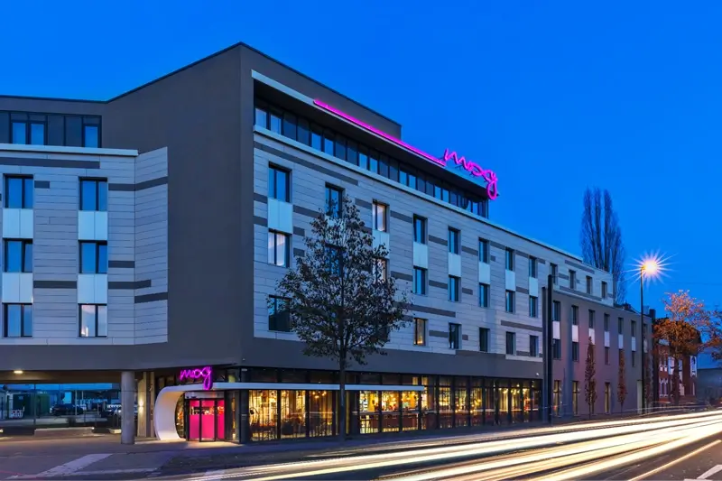 Moxy Hotels building illuminated with bold pink neon sign against a deep blue evening sky