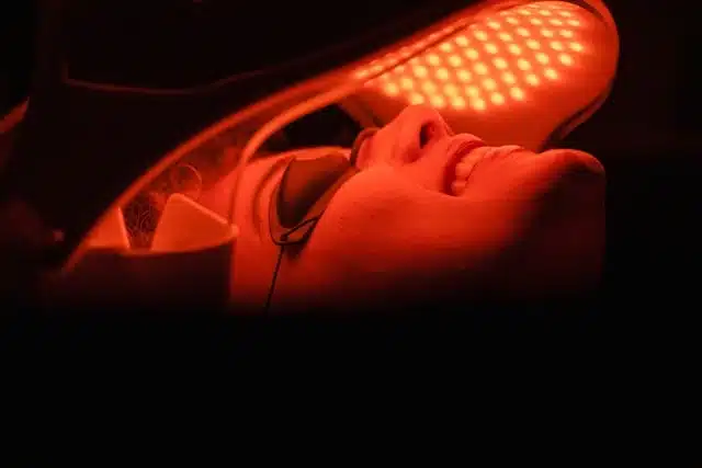 woman receiving red light therapy for hair growth under an LED panel device