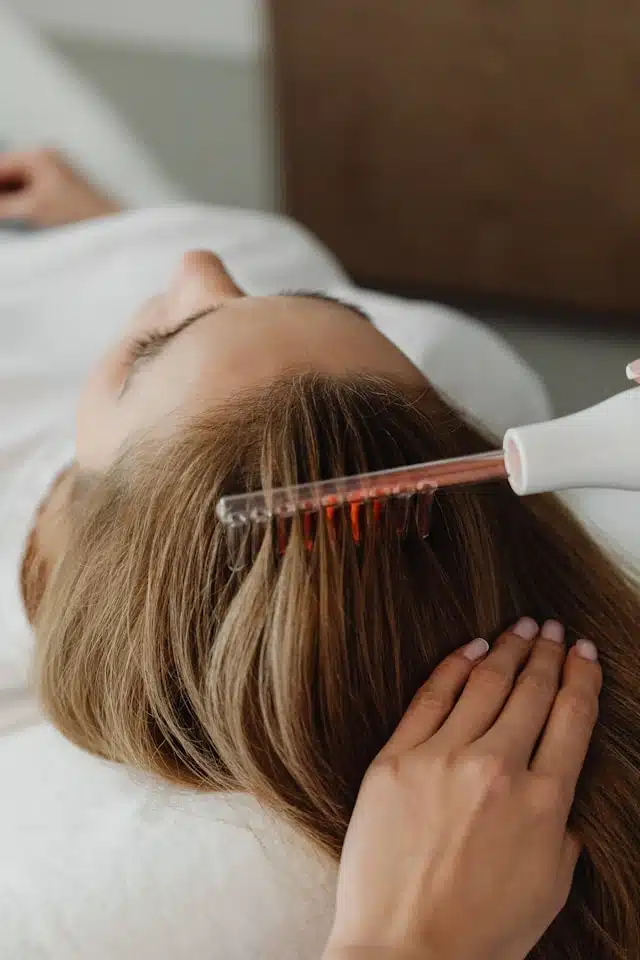 therapist applying a red light comb device to a woman's scalp during a hair regrowth treatment