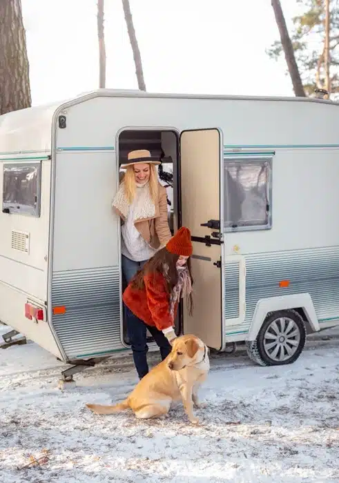 woman and child with a dog outside a campervan parked at a snowy rv campsite