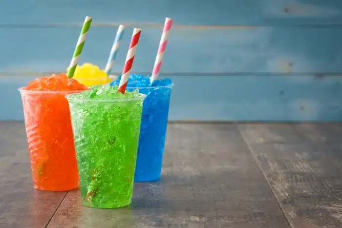 Three colorful slushie drinks in plastic cups with striped straws served at a commercial food business.
