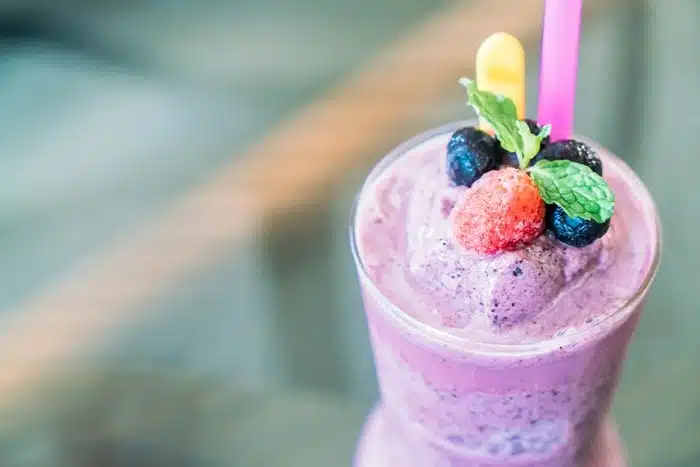 A beautifully presented berry slush drink topped with fresh strawberry, blueberries, and mint leaves in a glass.