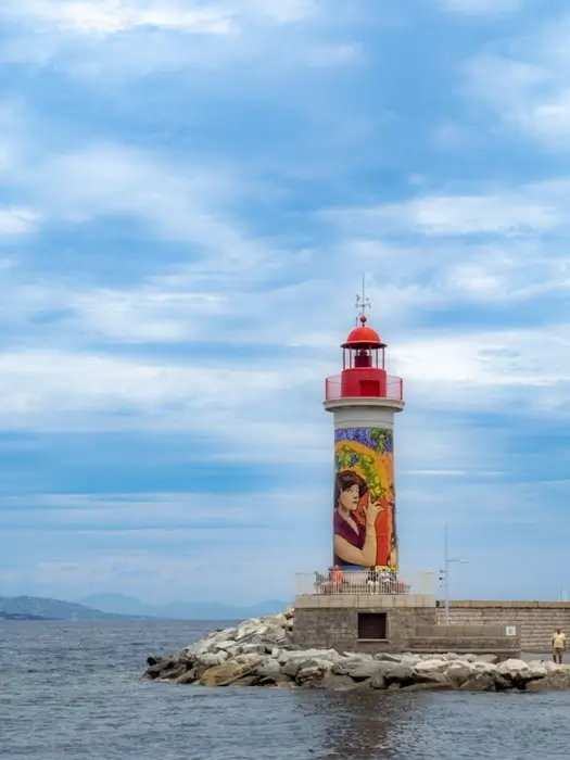 St. Tropez lighthouse with a colorful painted mural on the harbor jetty against a cloudy sky