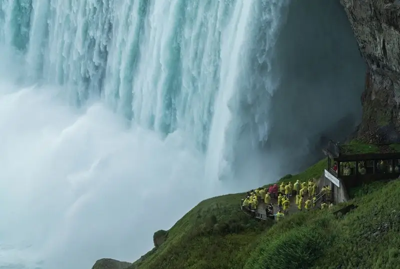 visitors in yellow ponchos standing on the outdoor observation deck below Horseshoe Falls in Niagara