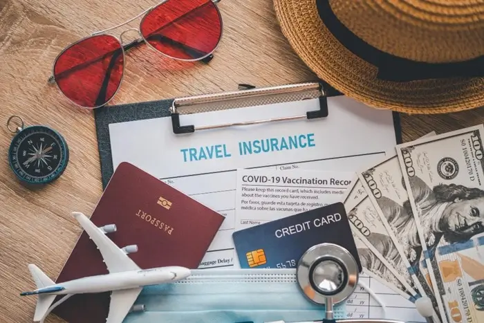 travel insurance form surrounded by passport, credit card, cash, and travel essentials on a wooden surface