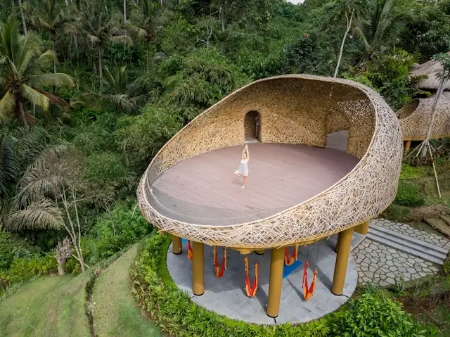 Woman practicing yoga in a stunning woven bamboo pavilion surrounded by lush jungle in Ubud, Bali