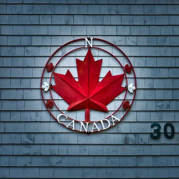 Red Canadian maple leaf compass sign mounted on a wooden shingle wall