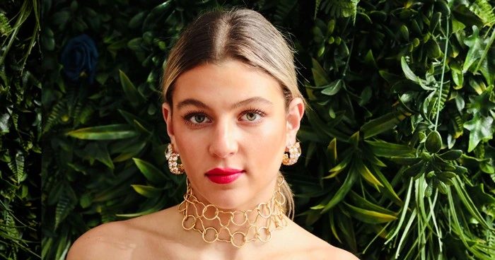 Woman wearing crystal stud earrings and a gold choker statement necklace against a green botanical backdrop