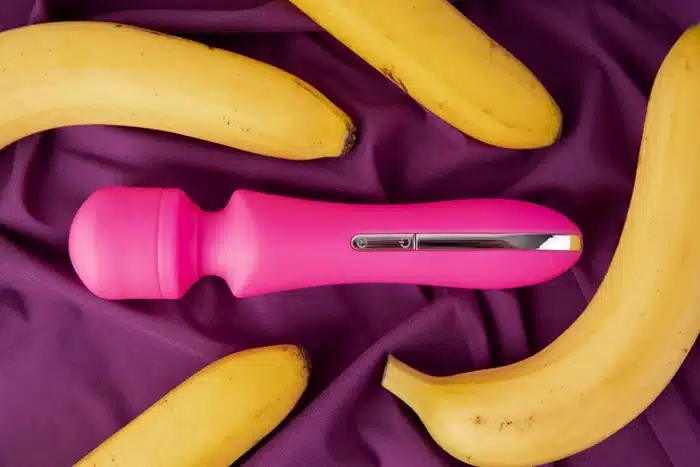 Pink wand vibrator surrounded by bananas on a purple fabric background