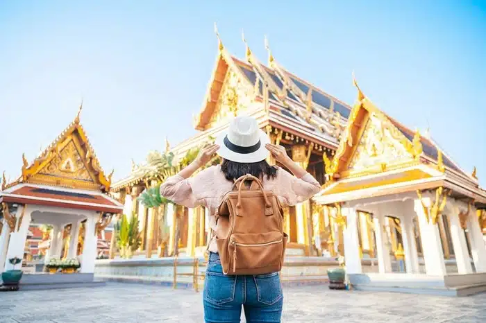 a first-time visitor with a backpack and hat standing in front of the Grand Palace in Bangkok