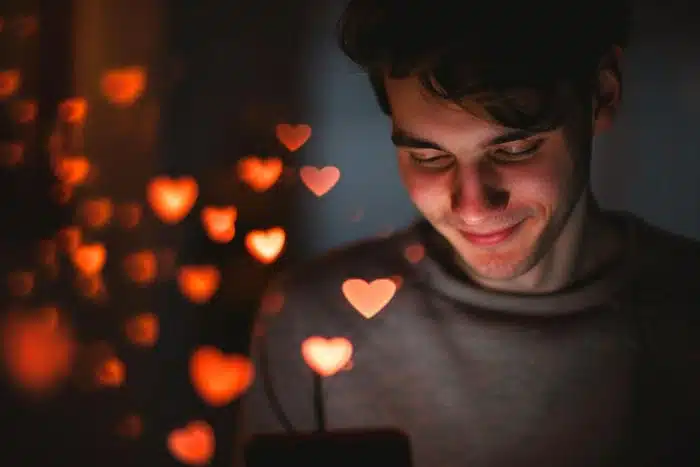 man smiling at his phone surrounded by glowing hearts while online dating