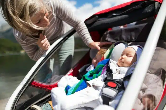 traveling with a newborn — mom checking on baby sleeping in a stroller by a mountain lake