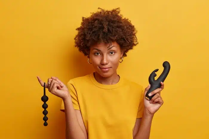 Woman holding two black silicone sex toys against a yellow background