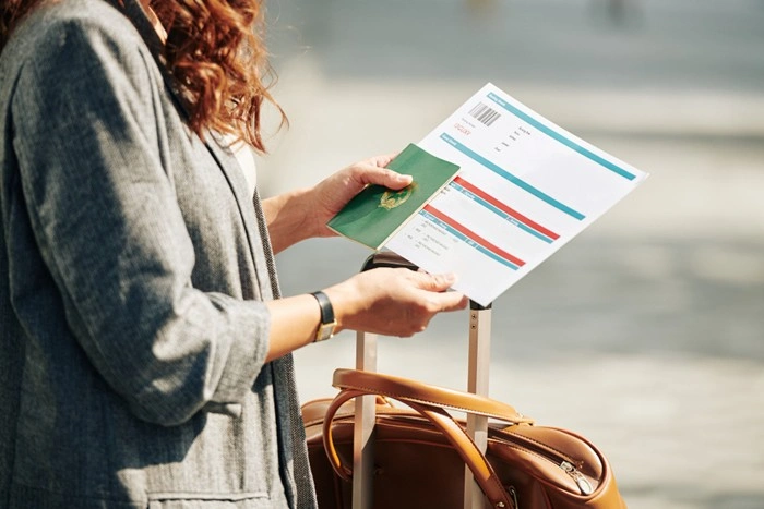 Woman reviewing a flight ticket and passport while standing next to luggage before a business trip