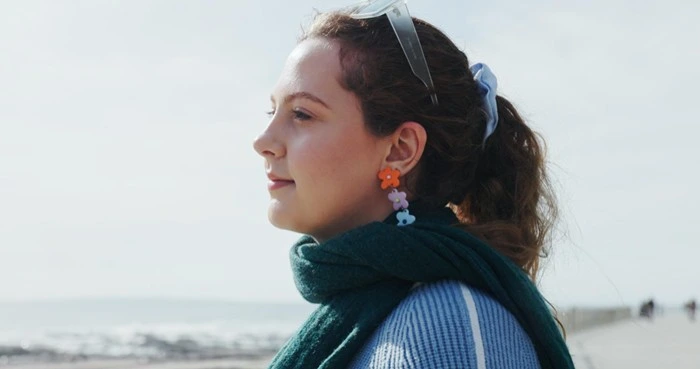 Woman at the beach wearing colorful floral stud earrings with a green scarf and casual blue top