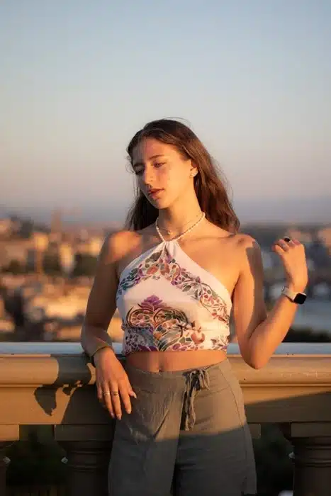 Woman in a printed halter top for warm-weather destinations, leaning against a stone balustrade with a Mediterranean cityscape at dusk