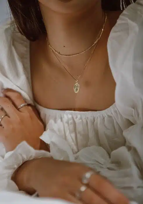 woman wearing layered gold virgin mary necklaces with a white linen top