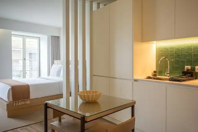 Compact New Zealand apartment interior with a kitchenette, glass dining table, and a separate bedroom area in the background