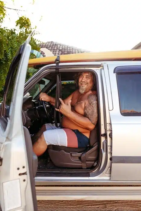 smiling man with tattoos sitting in a truck with a surfboard on the roof in Australia