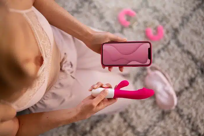 Woman using a smartphone to control a thrusting sex machine with app connectivity