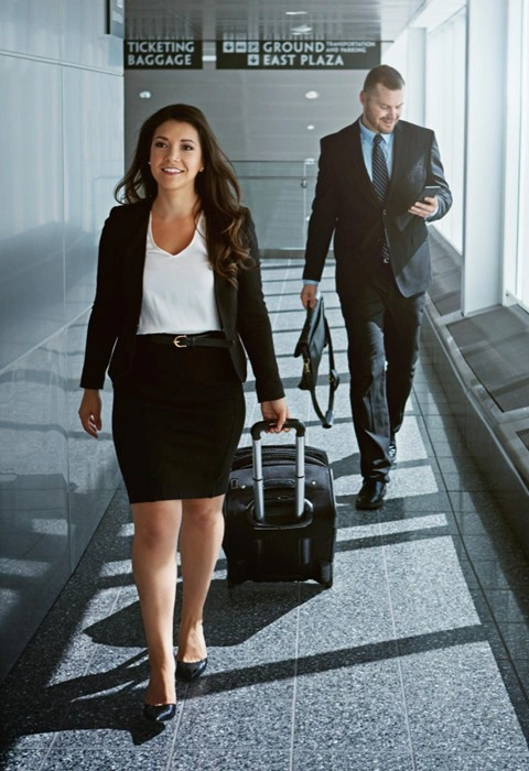 Two business professionals walking through an airport terminal with luggage, heading to their departure gate
