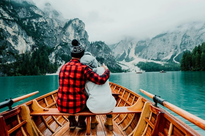 A couple embracing in a wooden rowboat on a turquoise alpine lake surrounded by misty mountains